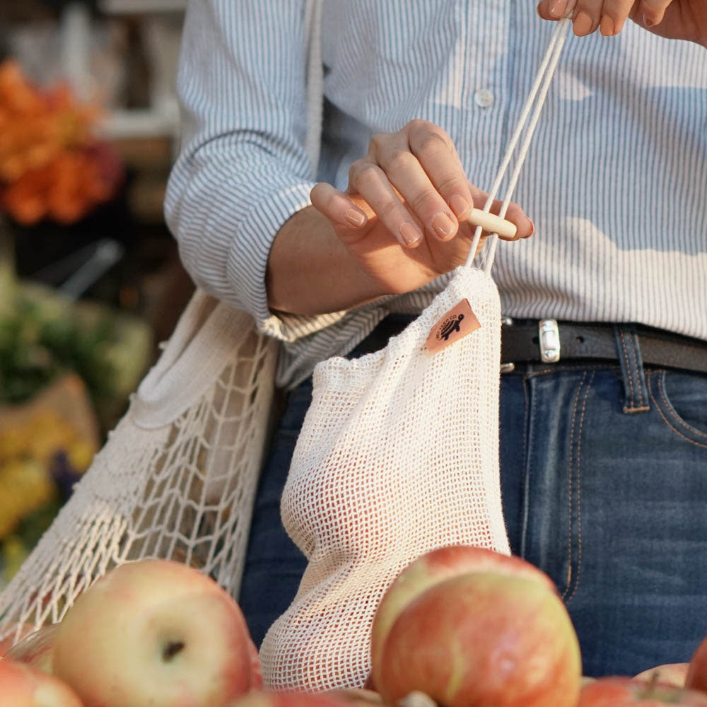 Woman using cotton mesh produce bag to store apples