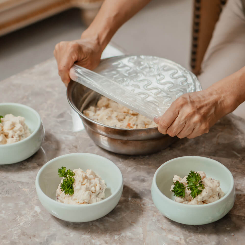 Hand using Large Silicone Stretch & Seal Lid to store potato salad without plastic.