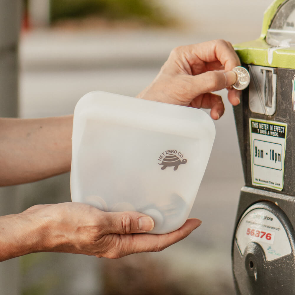 Hand putting coins into parking meter from pocket sized Silicone Zip Sealer storage.